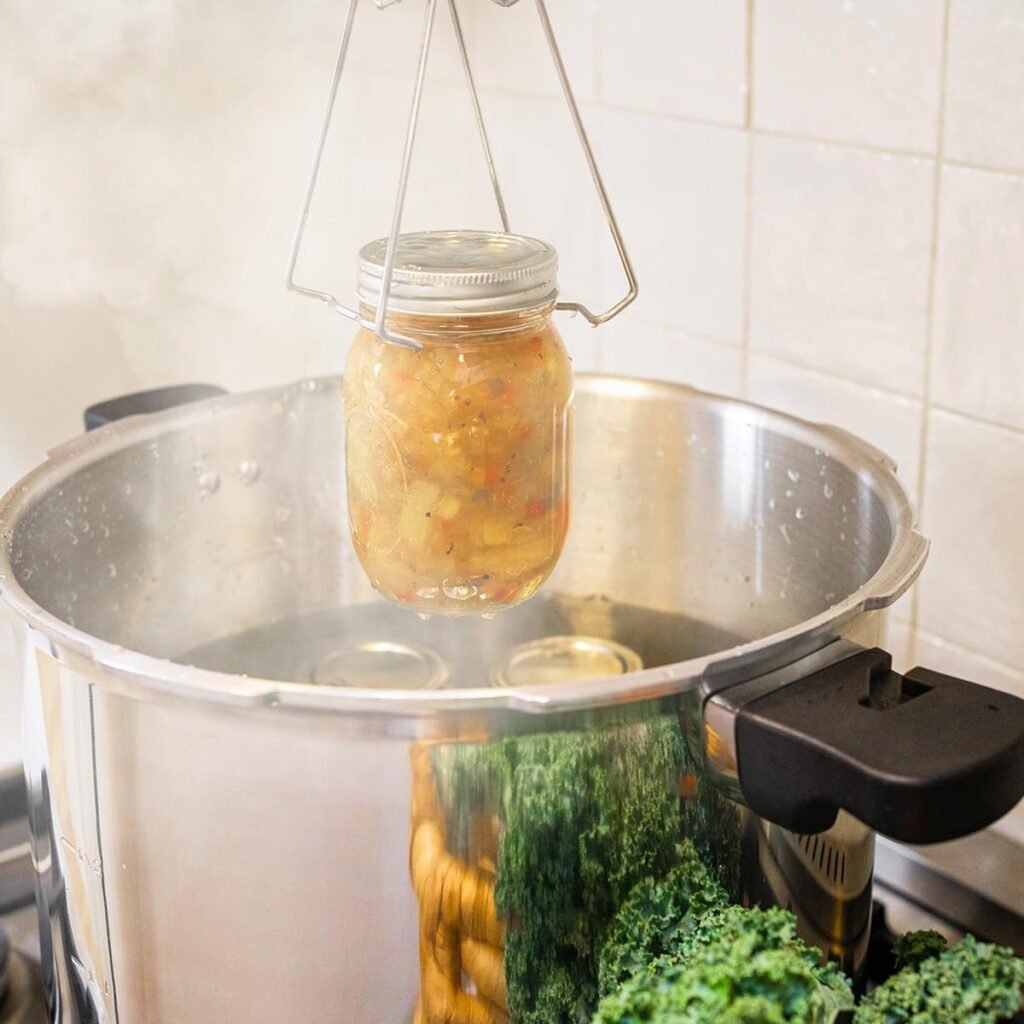 Glass jar being lifted from a stainless steel pressure cooker during the canning process in a home kitchen.