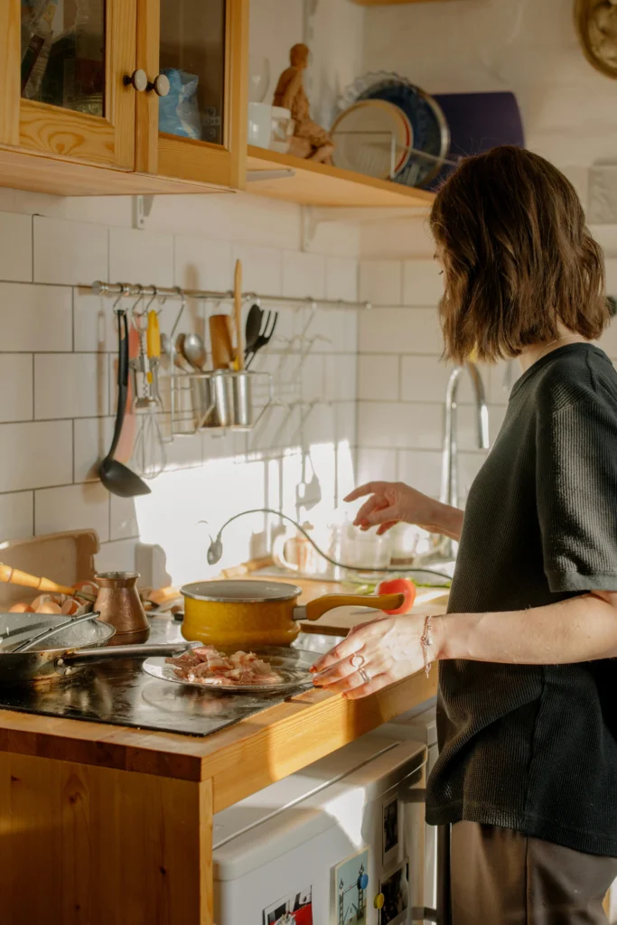 Woman cooking in a cozy kitchen using essential cooking tools for kitchen including silicone, stainless steel, and wooden utensils.